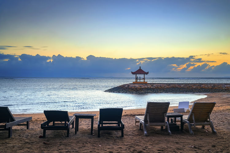 Chairs and table at beach against sky during sunset