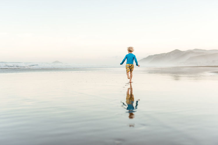 Toddler boy running on a beach with reflection