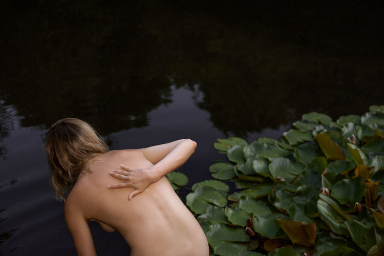 Rear view of naked woman bending in lake