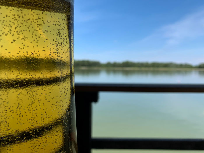 Close-up of beer glass on table against water in background