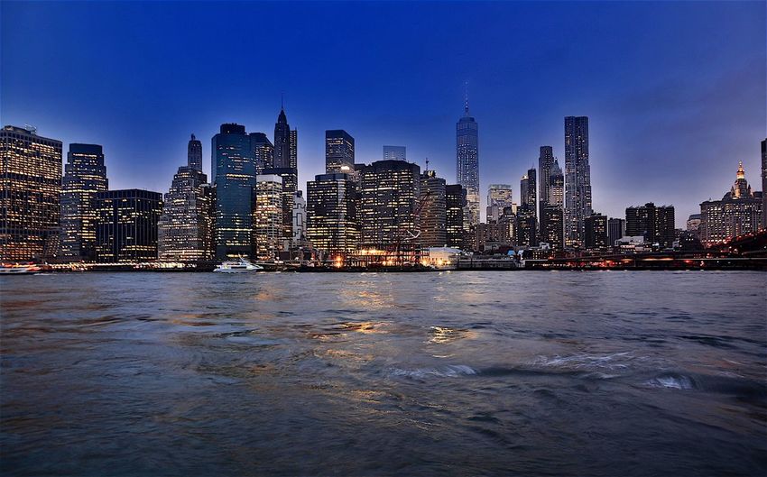 Scenic view of east river against illuminated buildings at dusk