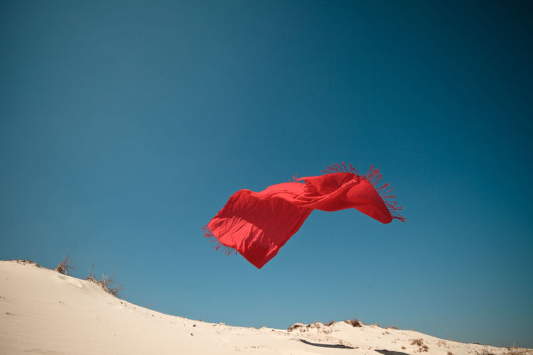 Low angle view of red scarf flying over sand against clear blue sky
