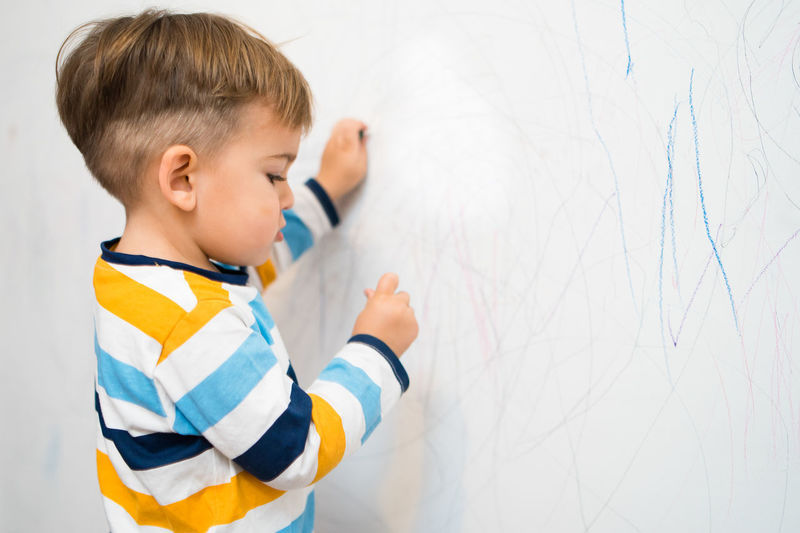 Cute boy drawing on wall at home