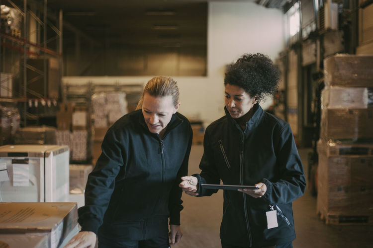 Female colleagues examining while holding digital tablet at distribution warehouse