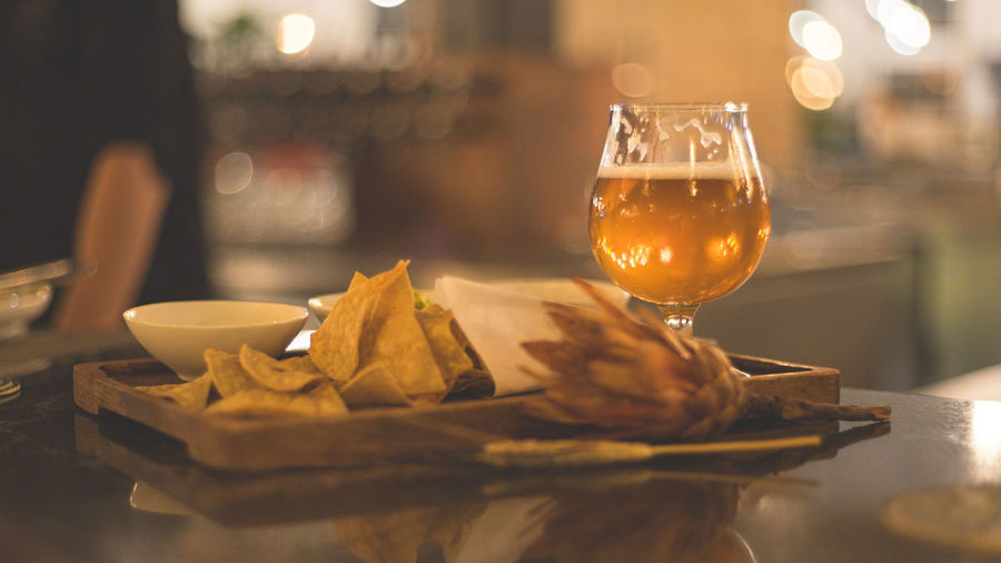 Close-up of beer glass with flower and nacho served on table