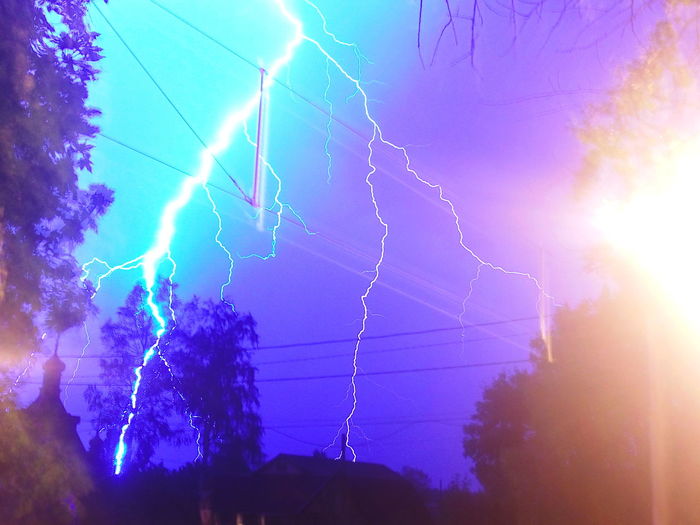 Low angle view of lightning over illuminated trees against sky