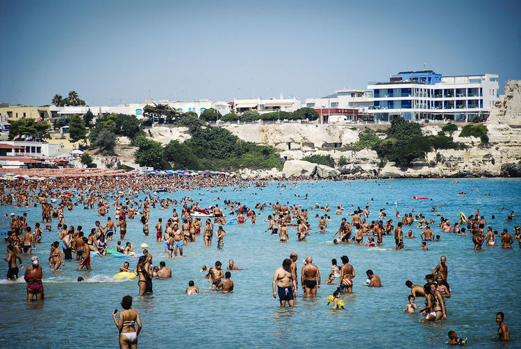 People by sea against clear blue sky