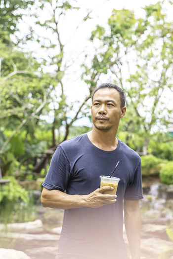 Man holding coffee while standing against trees