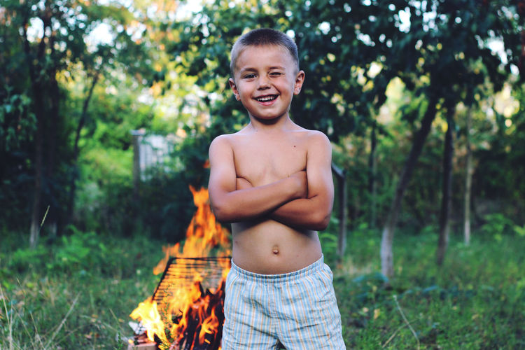 Portrait of happy boy blinking eye while standing against bonfire