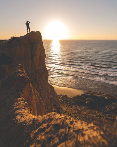 Woman standing on cliff against sea during sunset