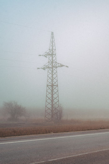Electricity pylon on field by road against sky