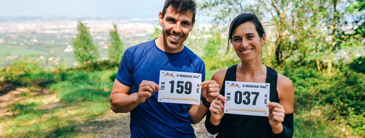 Portrait of happy couple holding marathon bibs while standing on field