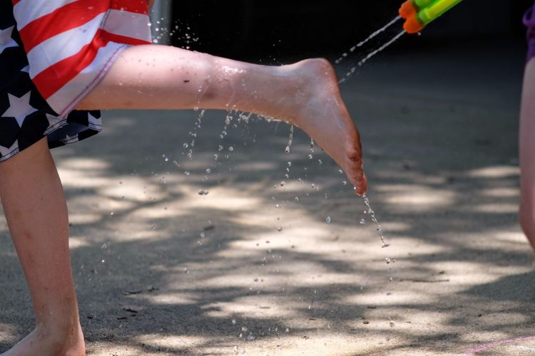 Low section of person washing legs with water splashing from squirt gun
