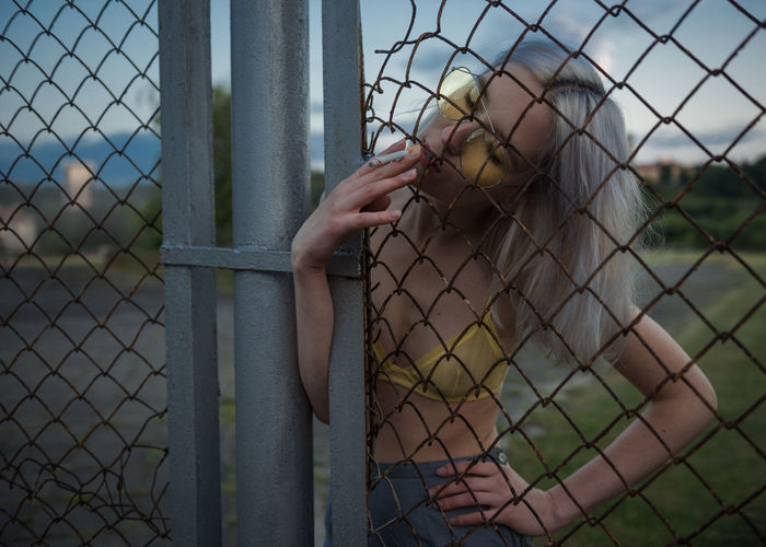 Portrait of young woman standing by chainlink fence