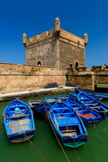 Blue boats moored in canal by castle against clear blue sky during sunny day