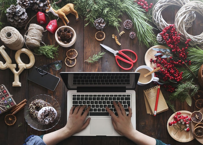 Woman working with laptop at her desk covered with utensils for creating advent wreaths, partial view