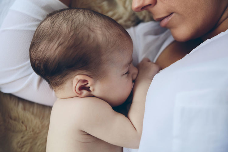 High angle view of mother breastfeeding daughter while lying on bed at home