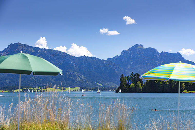 Parasols by lake forggensee against sky