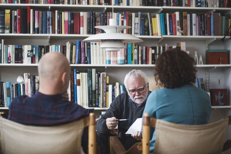 Senior therapist explaining analysis to mature couple against bookshelf at home office