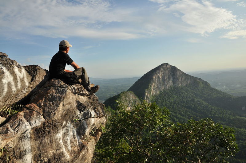 Man sitting on rock by mountain against sky