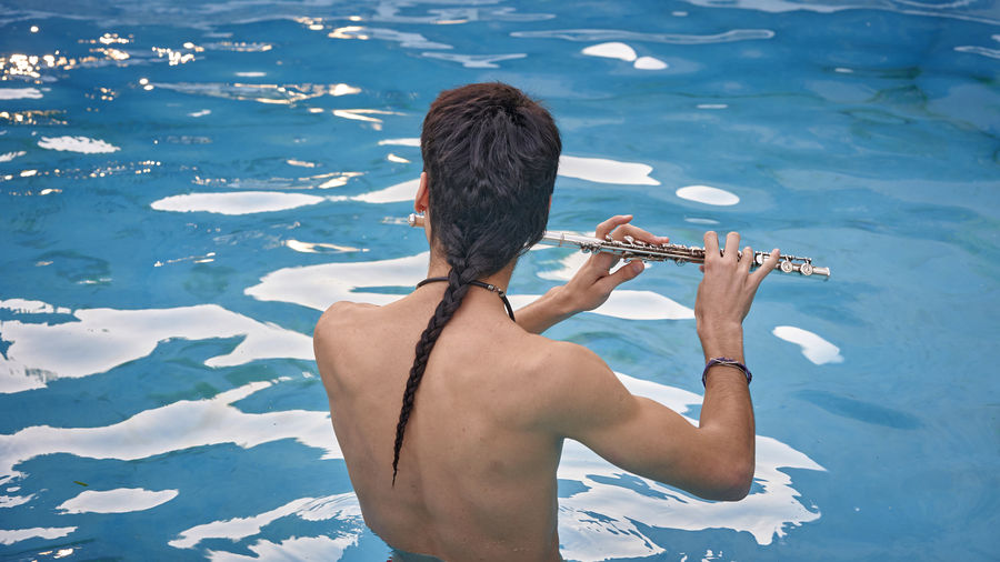 The young man relaxes plays flute on in an outdoor pool in the sun.