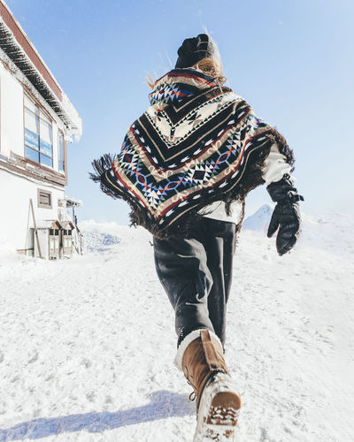 Man wearing poncho running on snow towards mountain hut