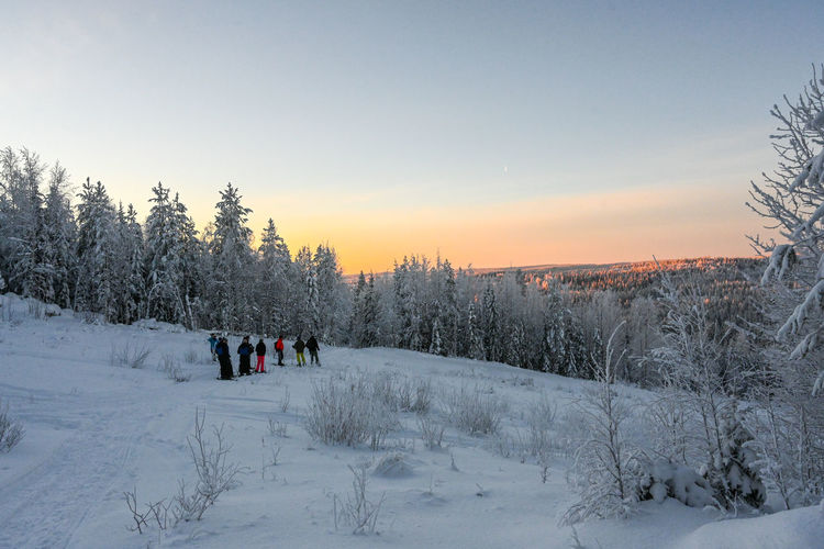 People on snow covered field against sky during sunset
