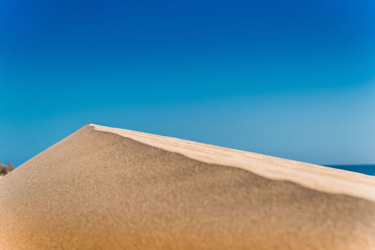 Low angle view of sand against clear blue sky