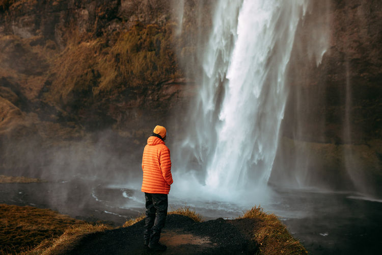 Rear view of man standing on rock looking at waterfall