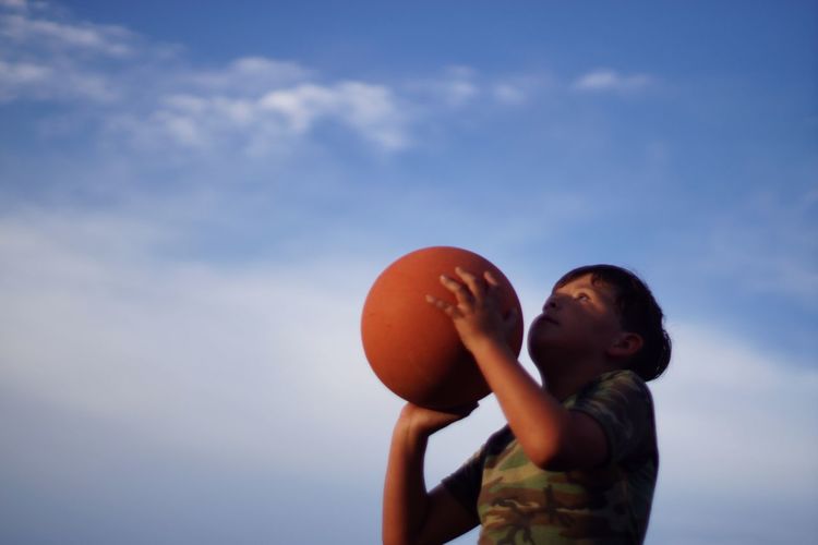 Low angle view of boy playing with basketball against sky