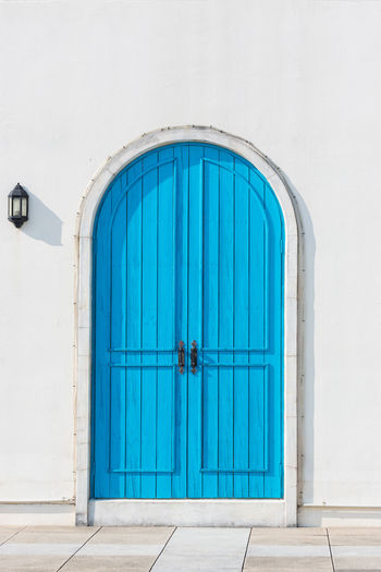Colorful wooden blue door and detail of house exterior on white wall.