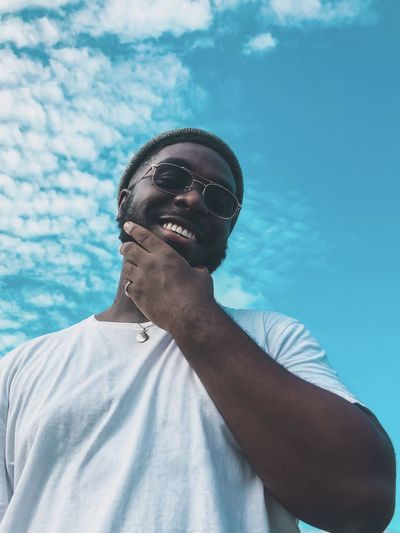 Low angle portrait of young man standing against blue sky