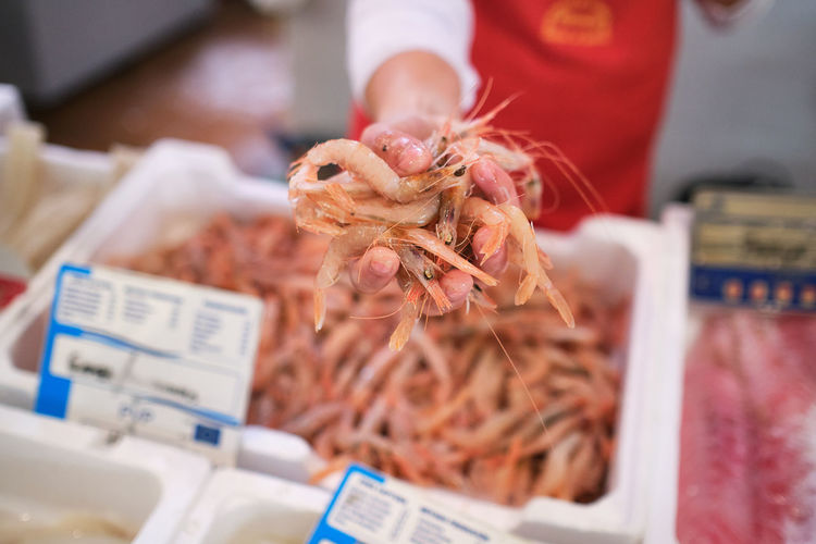 Young woman's hand teaches shrimp in the fish shop to her customers