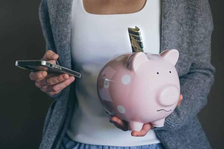 Close-up woman holding sad piggy bank and using mobile phone. female saving money.