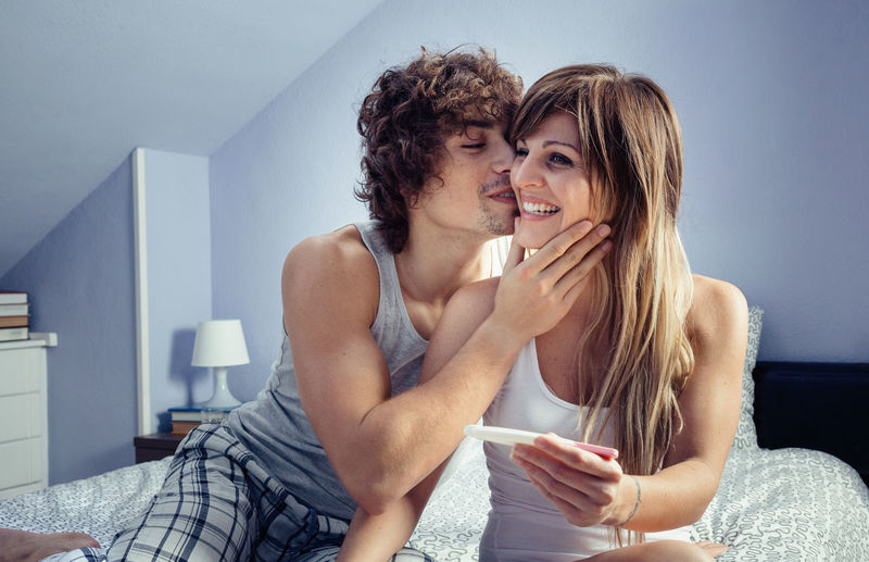 Cheerful couple with pregnancy test on bed at home
