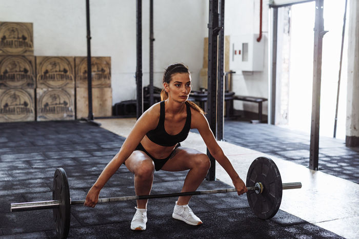 Young female athlete exercising with barbell in gym