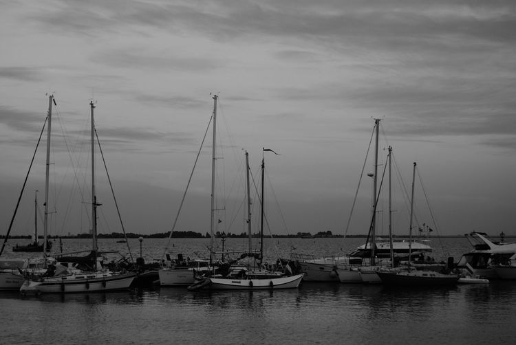Boats at harbor against cloudy sky