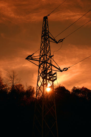 Low angle view of silhouette electricity pylon against sky during sunset