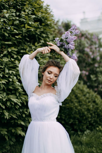 A beautiful delicate elegant young woman bride in a wedding dress walks alone in a blooming park