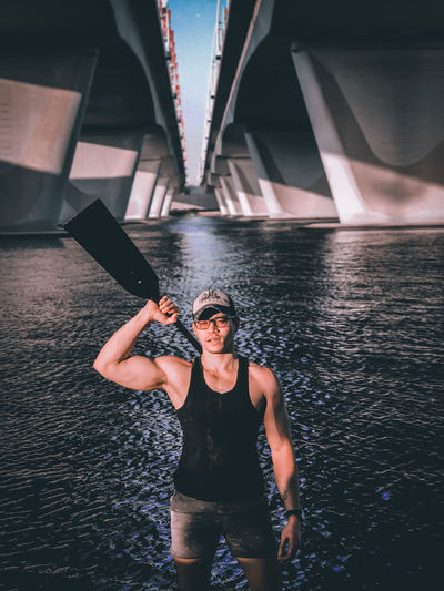 Portrait of man standing with oar under bridge