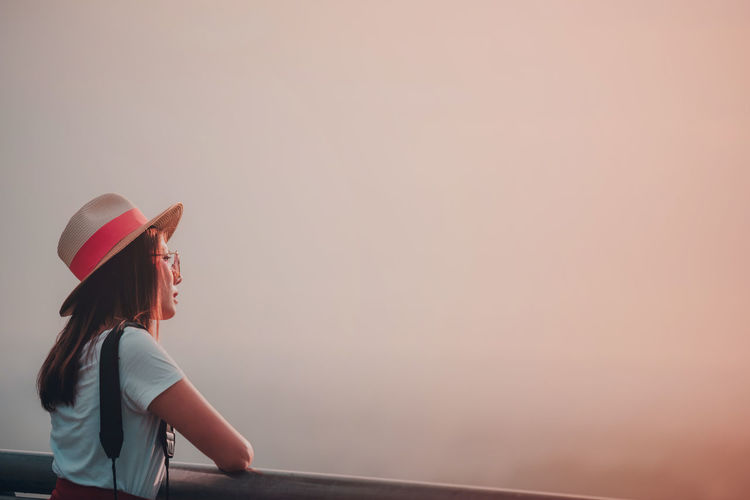 Side view of young woman looking away against sky