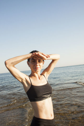 Portrait of woman standing at beach against clear sky