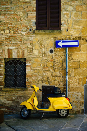 Yellow motor scooter by arrow sign on footpath by building