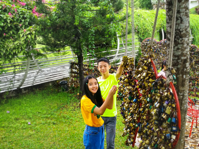 Smiling boy and girl standing by love locks against trees