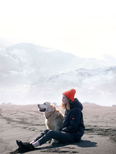 Young woman sitting with dog at beach during winter