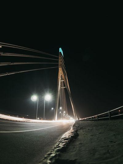 Illuminated bridge over road against sky at night