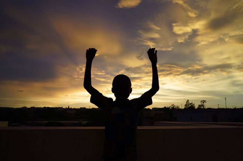 Silhouette boy standing against sky during sunset