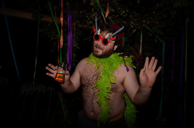 Shirtless man wearing feather boa while holding drink during party