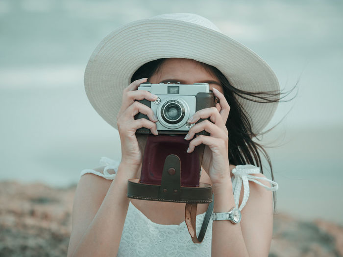 Close-up of woman photographing with analog camera against sky