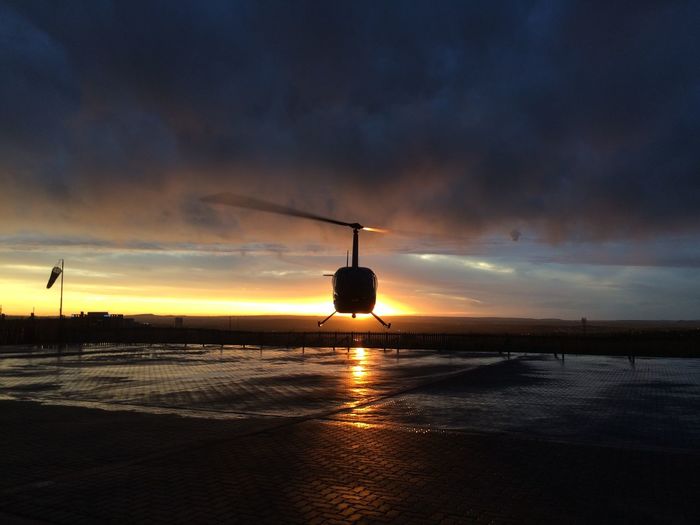 Helicopter flying over helipad against sky during sunset
